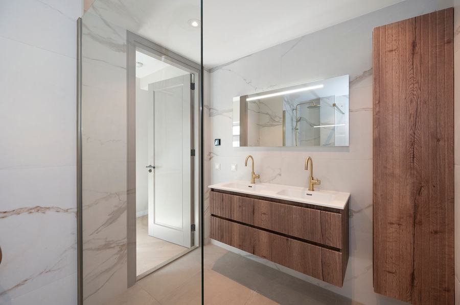 Badkamer met houten meubel, marmerlook en glazen douchewand